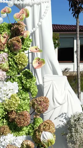 Elegant wedding arch on the podium with fabric, beads, candles, tiers and romantic floral arrangement in white and green tones. Amaranth, anthurium, hydrangea, rose, dahlia. Summer windy atmosphere.