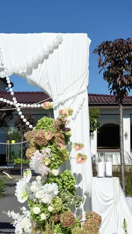 Elegant wedding arch on the podium with fabric, beads, candles, tiers and romantic floral arrangement in white and green tones. Amaranth, anthurium, hydrangea, rose, dahlia. Summer windy atmosphere.