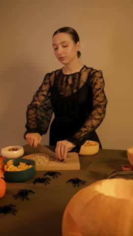 Woman chef chops nuts with a big knife on a kitchen board Autumn decorations and Halloween spiders complete the cozy scene