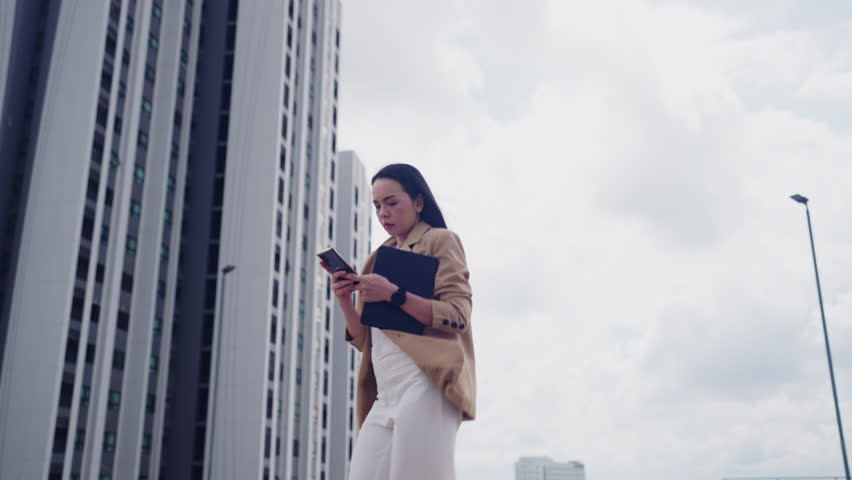 Confident Asian businesswoman walking in city holding smartphone and tablet. Urban professional female executive leader outdoors.