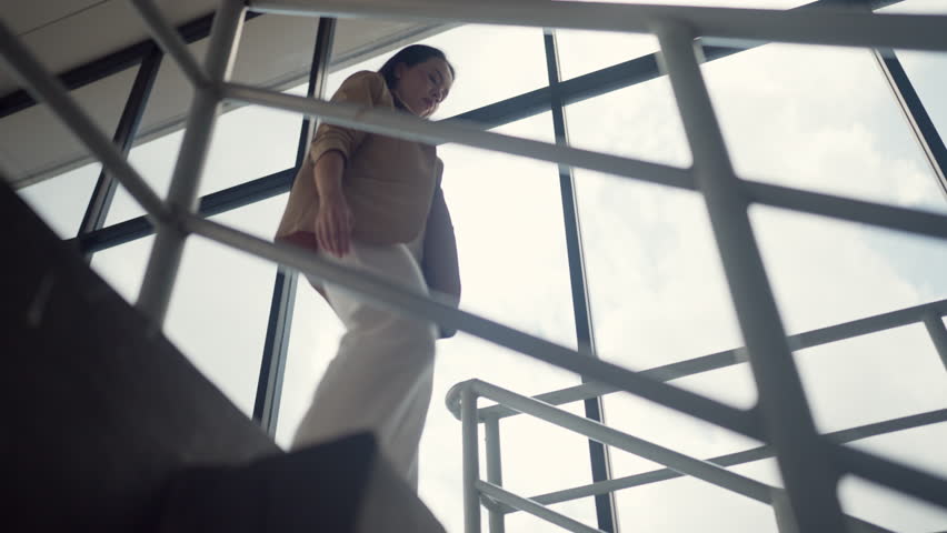 Businesswoman in beige blazer stepping down stairs confidently in urban area. Metaphor for forward movement and growth.