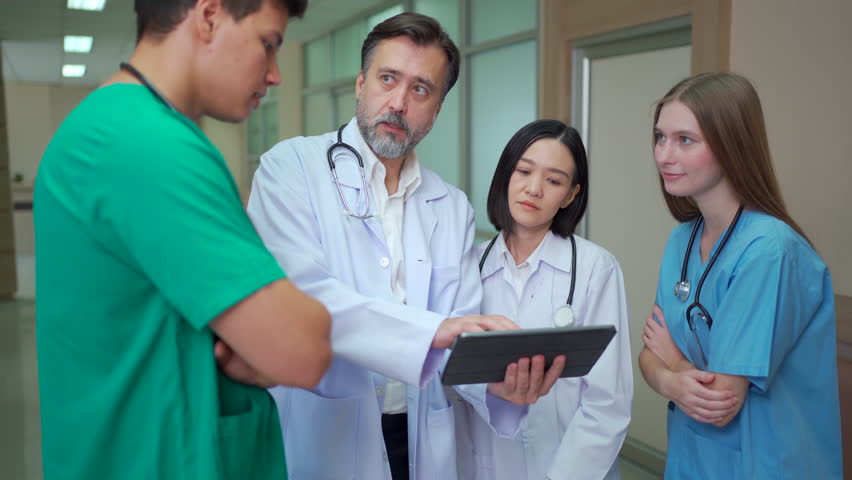Diverse team of doctors and medical professionals from different nationalities standing in hospital corridor, discussing healthcare data and explaining information on digital tablet with teamwork. - Powered by Shutterstock - Get 15% off with code: PIKWIZARD15