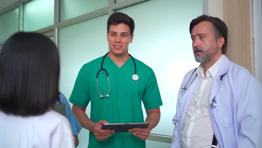 Diverse team of doctors and medical professionals from different nationalities standing in hospital corridor, discussing healthcare data and explaining information on digital tablet with teamwork. - Powered by Shutterstock - Get 15% off with code: PIKWIZARD15