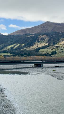 Camera pans across river, bridge, and mountains under daylight with soft, natural lighting