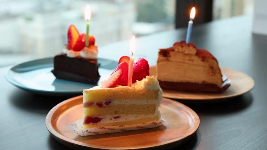 Three cakes with lit candles on plates, natural daylight, shallow depth, steady camera, celebratory mood
