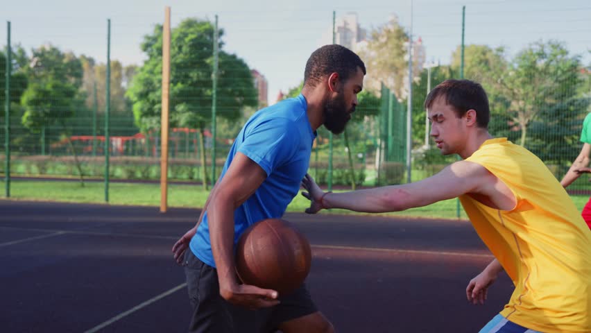 Portrait of skillful active sporty fit African American male basketball player receiving pass from teammate, making three points shot while multi ethnic athletes playing streetball on outdoor court. - Powered by Shutterstock - Get 15% off with code: PIKWIZARD15