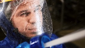 A close-up view of a worker cleaning equipment with a hose. The portrait of the man on dangerous chemical plant, wearing protective gear. The face is covered with a transparent mask screen - Powered by Shutterstock - Get 15% off with code: PIKWIZARD15