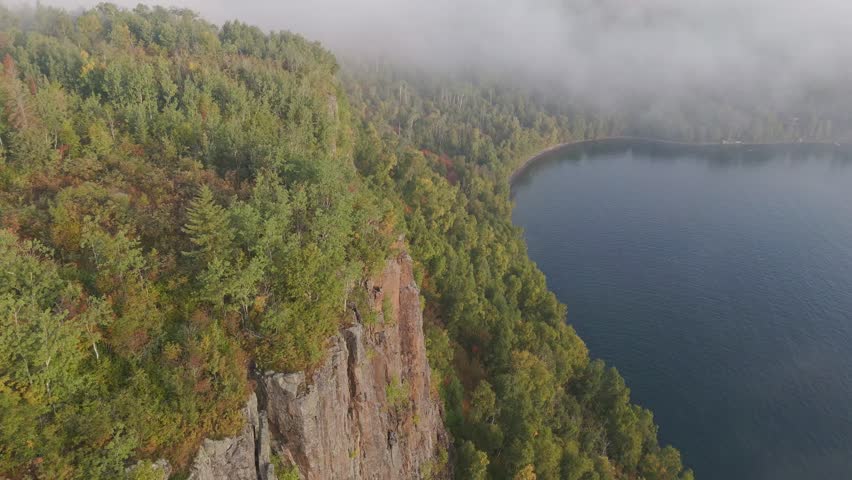 Sunlight illuminates Ontario’s wild Lake Superior shoreline, where bold cliffs rise above a forest glowing with early fall hues