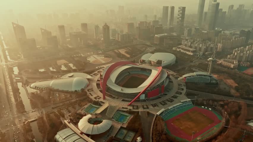 Aerial view of Nanjing Olympic Sports Centre Stadium at sunset in Nanjing, China, showcasing modern architecture, city skyline, and vibrant urban atmosphere.