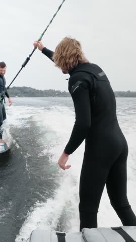 Two Surfers Engaging in an Exciting Water Sport Adventure, Riding the Waves on a Surfboard While Being Towed by a Boat, Capturing the Thrill of Water Sports