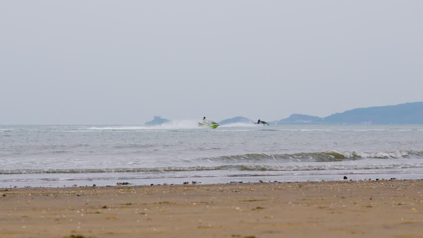 Jetski Riding Along Calm Sea in Swansea Bay with Mumbles in Background on Overcast Day in Winter.