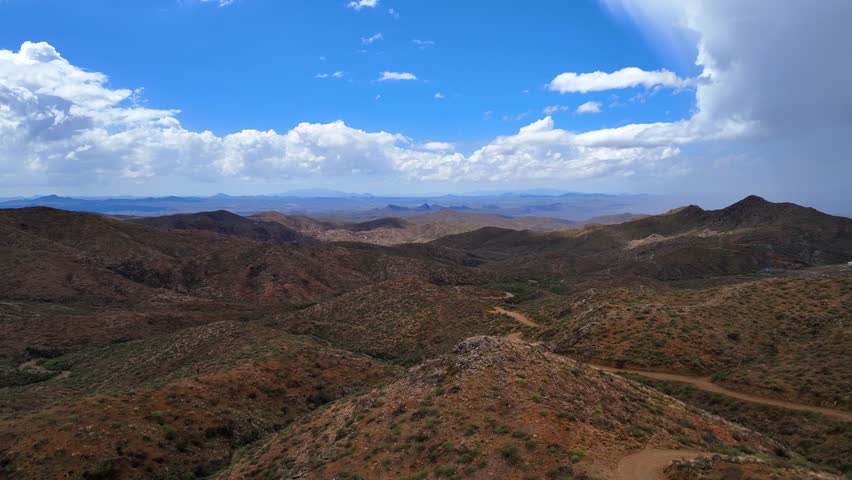 Aerial view of the desert mountains, rugged terrain, and winding dirt trails under a partly cloudy sky with sunlight and shadows, Wickenburg, Arizona, United States.