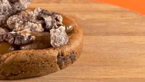 Close-up of a delicious cookie topped with caramel, cream, and sugared pecan, displayed on a rotating wooden plate with an orange background. - Powered by Shutterstock - Get 15% off with code: PIKWIZARD15