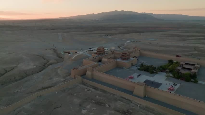 Aerial view of the Jiayu Great Wall Fort, a beige fortification contrasting with the surrounding arid landscape under a soft, muted sky, Jiayuguan, Gansu, China.