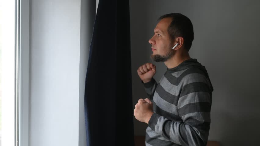 A bearded middle-aged man listens to music on headphones at home with emotion. 