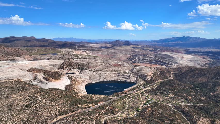 Aerial view of a vast open pit mine with a deep blue lake contrasting with the arid landscape, Globe, Arizona, United States.