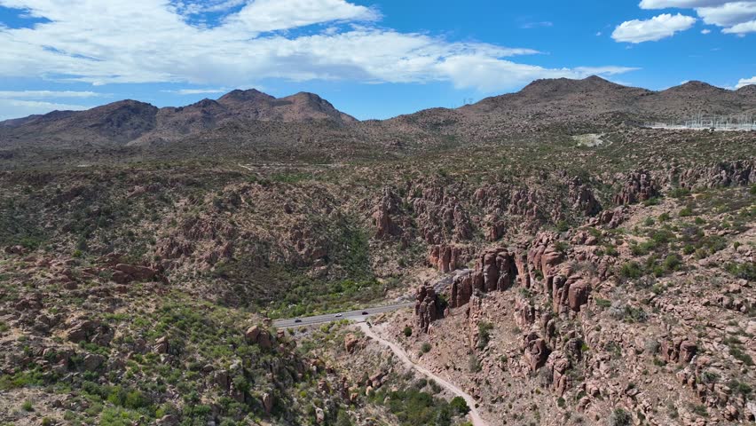 Aerial view of rocky mountains and a road winding through the arid landscape under a vast blue sky with scattered clouds, Globe, Arizona, United States.