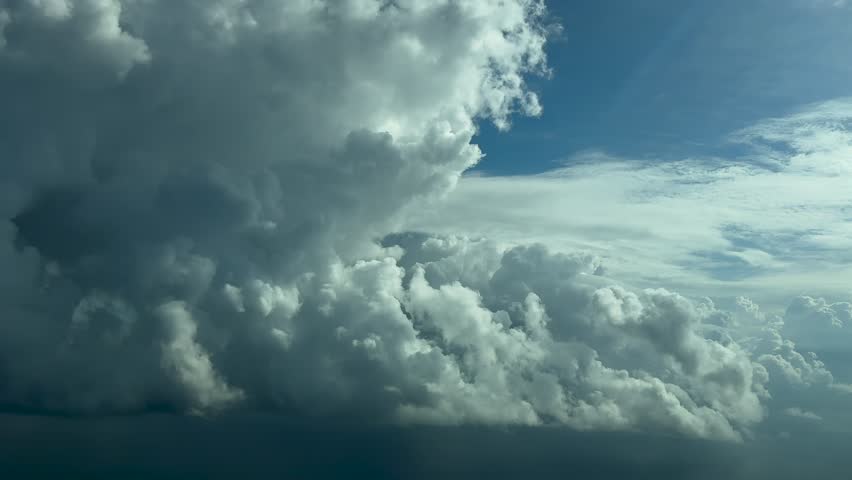 A peaceful flight experience flying near a massive cumulonimbus storm cloud, in a turbulent bright blue sky as seen by the pilot from a jet cockpit.