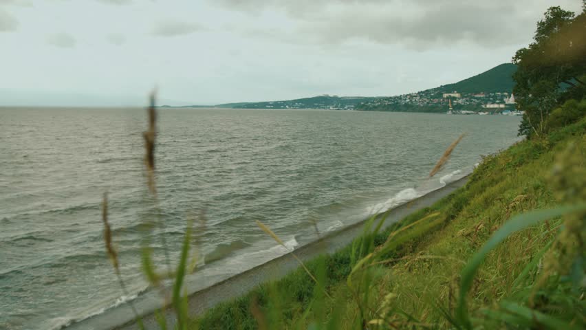 View from hill across wind-blown grass to blurred view of sea bay