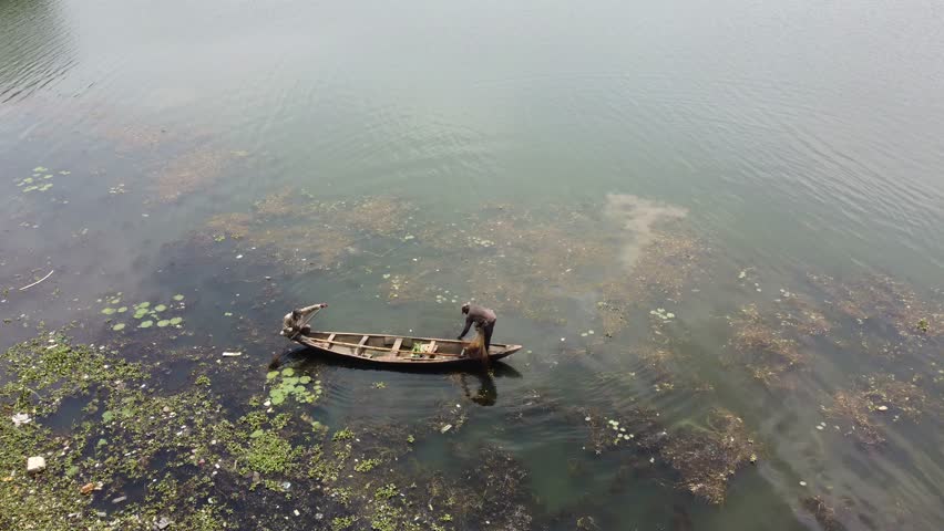 Abuja, Nigeria - 10 October 2025: Aerial view of boat carrying two people on Alex Ekwueme Way, surrounded by green aquatic plants and murky water.