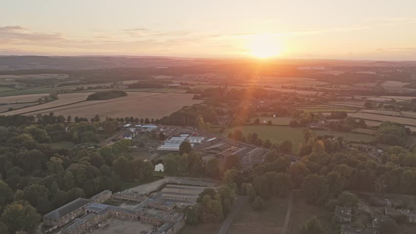 Aerial drone view of Wentworth village in South Yorkshire, England, showing historic buildings, fields, and trees under a warm golden sunset that bathes the countryside in soft evening light