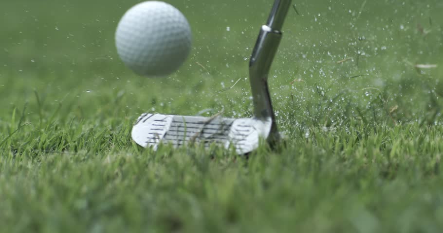 Golf club hits a white golf ball in a super slow motion. Drops of morning dew and grass particles rise into the air after the impact. Shot on super slow motion camera 1000 fps.