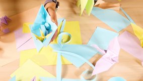 Hands organize pastel origami flowers and paper crafts on a well-lit wooden tabletop, overhead view - Powered by Shutterstock - Get 15% off with code: PIKWIZARD15