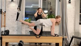 A Pilates instructor guides a student performing an advanced balance exercise on a reformer. The realistic frame captures concentration, alignment, and trust in professional body training. - Powered by Shutterstock - Get 15% off with code: PIKWIZARD15