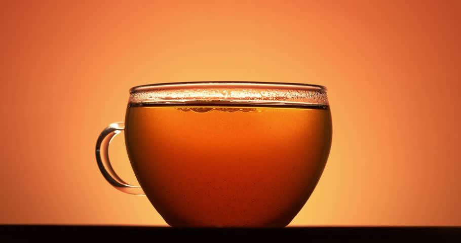 Hand picks up a transparent cup of tea, backlit footage.