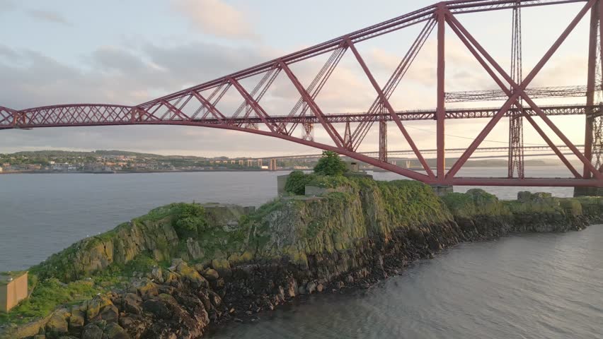 Aerial view of island ruins and seagulls beneath the red bridge in warm evening light