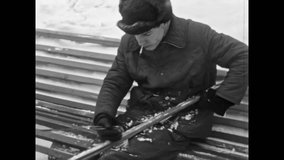 Man clears packed snow from skis on winter bench, preparing equipment for crosscountry ride. Active leisure, gear care, fitness sport in cold nature. Vintage film. Old archive. Archival retro 1960s - Powered by Shutterstock - Get 15% off with code: PIKWIZARD15