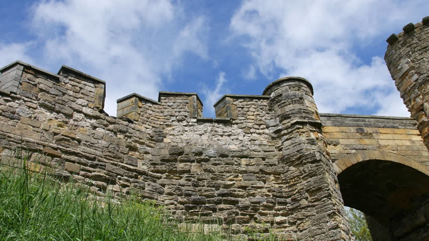 Stone castle walls with battlements and towers rise in Scarborough, North Yorkshire, England, viewed from below against blue sky and white clouds