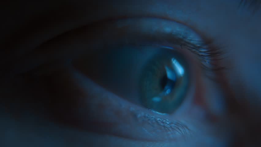 A macro view of wide-open human eye madly staring at a glowing phone screen late at night illuminated by blue light. Digital addiction social media dependence and excessive content consumption. 