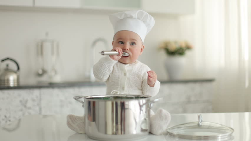 Little chef sitting in front of pan with spoon and eating something
