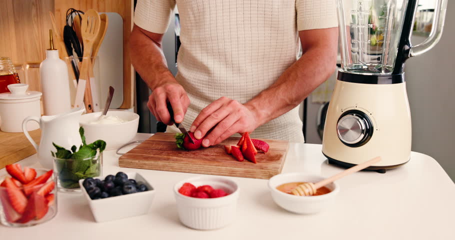 Hands, cut strawberry and blender on kitchen counter for healthy smoothie, nutrition and vegan diet. Man, chop fruit or ingredients in home with machine for drink, gut health or antioxidant benefits.