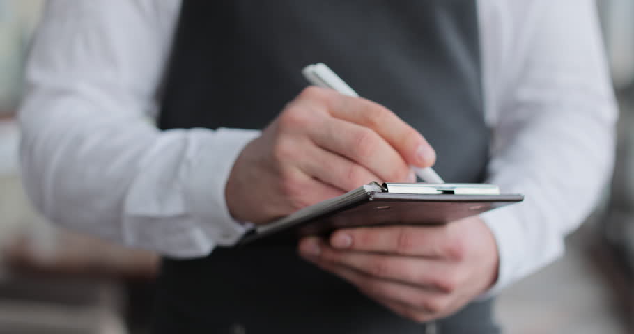 Close-up of a notebook in the hands of a waiter. A waiter down an order in a notebook in a restaurant.