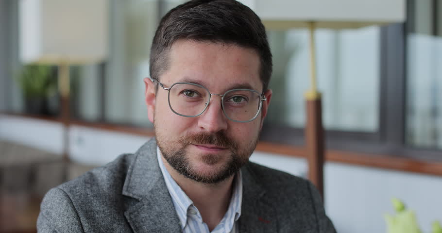 Portrait of a bearded man with glasses in a cafe. Man sitting at the table looking at the camera and smiling. Happy man, customer and breakfast in restaurant, enjoy.