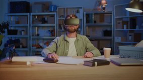 Bearded Man Wearing Virtual Reality Headset While Sitting At Desk With Laptop And Papers. Concept of Digital Innovation, Future Technology, VR Simulation, Remote Work, and Virtual Experience. - Powered by Shutterstock - Get 15% off with code: PIKWIZARD15