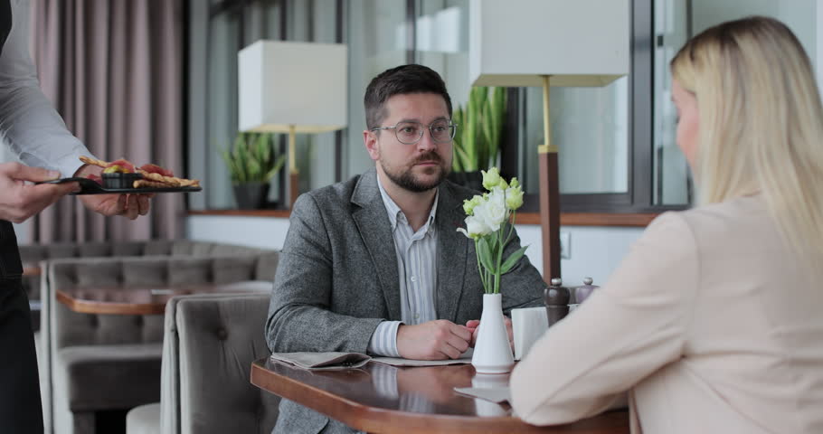 Waiter brings order for couples in restaurant. Couple sitting by table in a cafe. Customer service.
