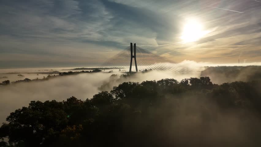 Aerial view of Redzin Bridge (Most Rędziński) in Wroclaw, Poland, surrounded by morning fog and forest under dramatic sunrise sky – scenic drone landscape of autumn mist and architecture