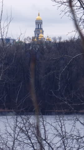 Beautiful view of the Kyiv Pechersk Lavra, a historic Orthodox Christian monastery, with its golden domes rising above the forest and reflecting in the Dnipro river on an overcast day
