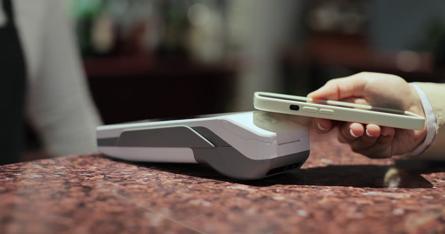 Purchase by smartphone on card reader. Pos-terminal in hand of waiter worker close-up. Modern technologies and restaurant business concept.