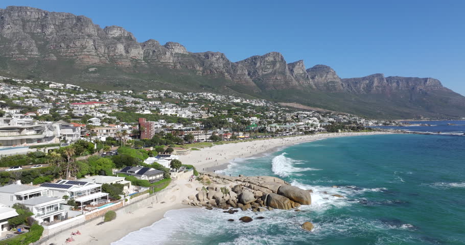 Aerial tilt up shot of Camps Bay beach on a sunny day in Cape Town, Western Cape, South Africa. 