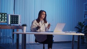 Neurology Consultation. Professional Female Doctor in White Coat Reviews Brain Scans During Evening Online Meeting, Providing Expert Analysis and Collaboration in Remote Medical Practice - Powered by Shutterstock - Get 15% off with code: PIKWIZARD15