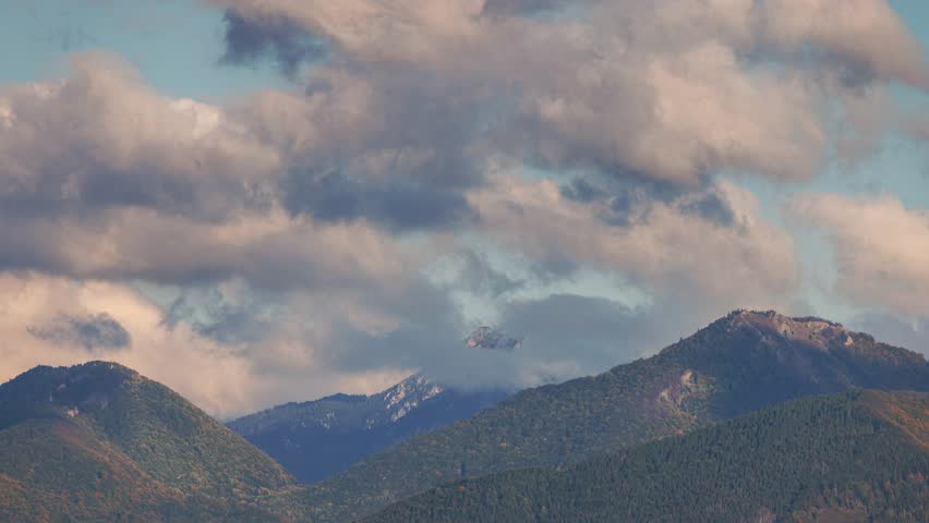 Mountains under a cloudy sky. Rolling hills with forestation are capped by gray cumulus clouds against a light blue sky background. The Mala Fatra national park in Slovakia, Europe. Timelapse footage.