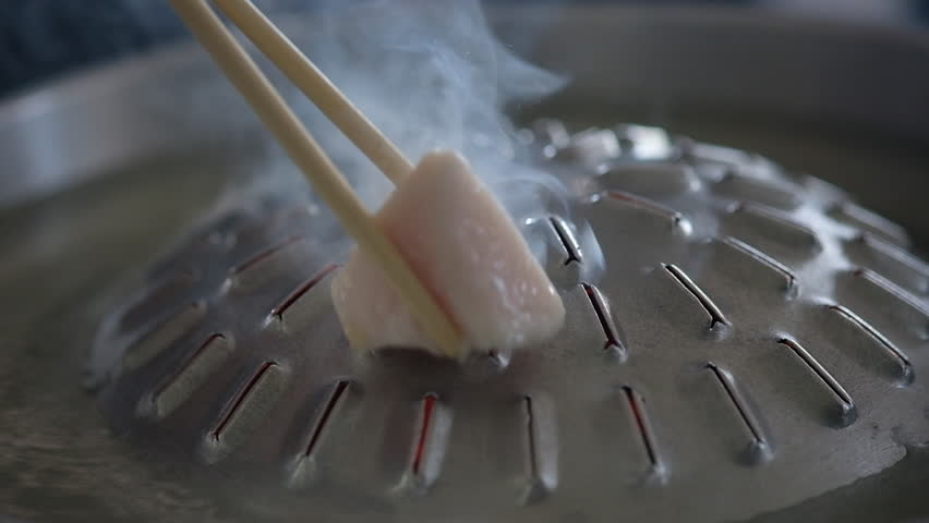 Close up use wood chopsticks to place pork fat cubes in a hot brass instead of oil preparation for cooking Thai grilled pork