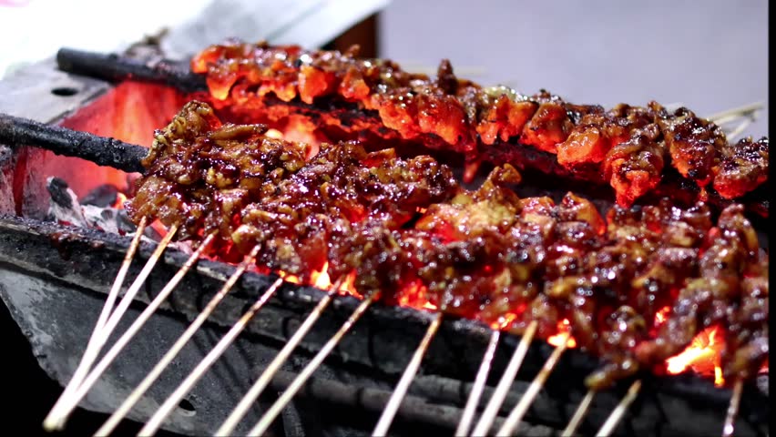 Chicken Satay or Sate Ayam skewers coated in thick peanut sauce, being grilled over glowing charcoal embers on a street vendor
