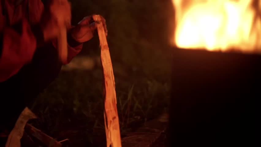 Man cutting wood with a machete near a campfire at night, creating a warm and cinematic atmosphere. Perfect for outdoor, survival, or camping themes.

