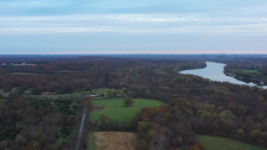 Aerial footage pulling back over rural farmland near Poolesville, Maryland, revealing the winding Potomac River and distant views of Northern Virginia beneath soft autumn skies.