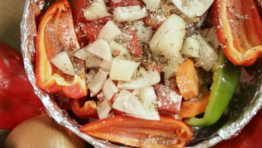 Male hand sprinkles dried garlic over chopped vegetables in baking dish. Bell pepper, tomato, onion and carrot form vibrant contrast. Concept of food styling, culinary texture and visual storytelling.